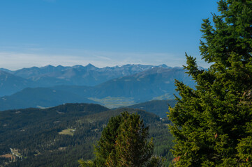 Bergige Landschaft in Österreich.  Blick von einem hochgelegenen Punkt auf  eine Gebirgskette im Vordergrund befinden sich Nadelbäume.  Sonniger Herbsttag