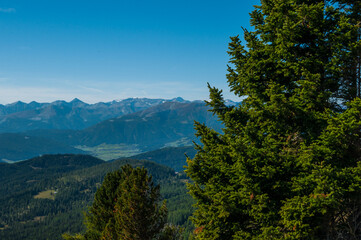 Bergige Landschaft in Österreich.  Blick von einem hochgelegenen Punkt auf  eine Gebirgskette im Vordergrund befinden sich Nadelbäume.  Sonniger Herbsttag