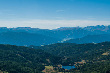 Bergige Landschaft in Österreich.  Blick von einem hochgelegenen Punkt auf  eine Gebirgskette und einem kleinen See im Tal. Sonniger Herbsttag