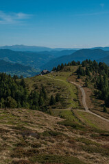 Bergige Landschaft in Österreich . Blick über eine Weide  auf einen Weg, der zu einer Jausenstation führt.  Sonniger Herbsttag