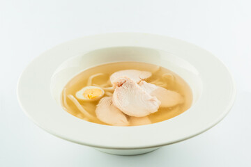 Classic Chicken broth with quail eggs and wheat noodles. Chicken soup stock served in white plate. First dish consomme isolated on white background
