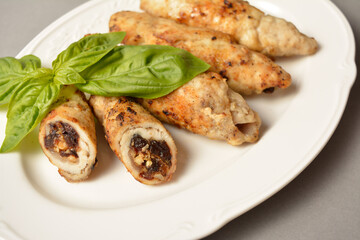 Meat roll with dried apricots, prunes and walnuts inside. Chicken Meat cannelloni stuffed with dried fruits and nuts. Served with fresh basil leaf on white vintage plate on gray solid background 
