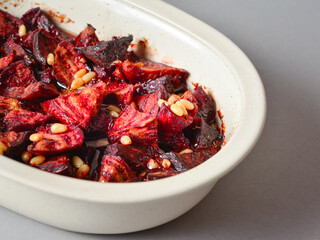 Baked beetroot with pine nuts in soy and honey sauce. Served in baking mold dish on gray background. Selective focus 
