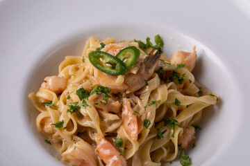 Italian pasta with prawns chili pepper and greens. Italian food, white dish, dark background