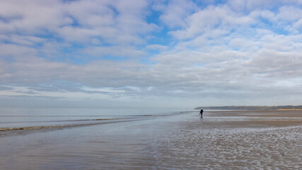 Fototapeta na wymiar Fin de matinée sur la plage à marée basse : calme et douceur d'une promenade dans une ambiance bleutée entre ciel et mer.