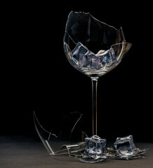 Close up of broken wine glass and ice cube on black background for food and drink design, Parts of the broken glass on floor with water Splash, The concept of danger. Nightlife scene with copy space