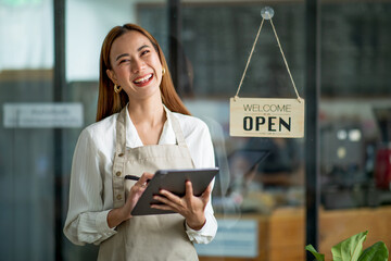 Asian Happy business woman is a waitress in an apron, the owner of the cafe stands at the door with a sign Open waiting for customers. Small business concept, cafes, and restaurants 