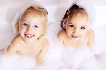 Two kids little girls sisters having fun in bathroom playing with bath foam. Kids personal care