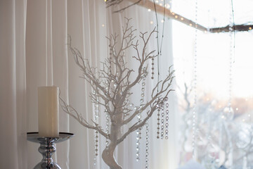 Christmas decorations on the window. White tree, candle and crystals on the background of curtains