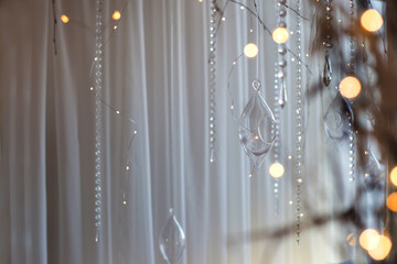 Shiny crystals on threads and Christmas lights on white tulle background. Home decorations