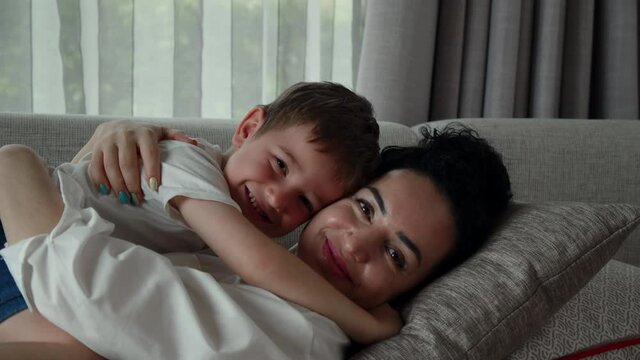 A happy family of mom and a son, resting together on the couch, these preschoolers sleep on their mother's tummy, hugging at home, the mother stroking the child on the head.