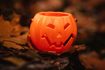 Halloween decor toy in the form of a pumpkin in the autumn forest on a tree stump