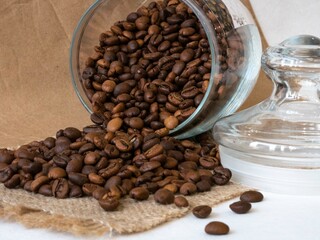 Coffee beans are spilled on the table from a glass jar. The bank is on the table. Roasted coffee for grinding