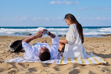 Young multicultural couple lying on the beach using smartphones