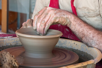 Hands of a caucasian  potter shaping a clay pot on a fast rotating potters wheel.