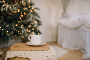 Cup of coffee on a stand in the bedroom on the background of the bed and Christmas tree