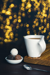 Obraz na płótnie Canvas White cup of tea with spoon and chocolate candy on blurred background with christmas lights