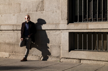 Adult man in suit standing on street against wall with sunlight and shadow