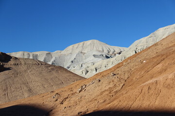 Red and brown slopes of the sandy-clay mountains Ak-Tau in Altyn-Emel, behind the slopes you can see a white ridge with peaks, clear sky, summer, sunny