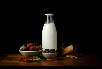 Still life of berry fruits on wooden table with bottle of milk against black background
