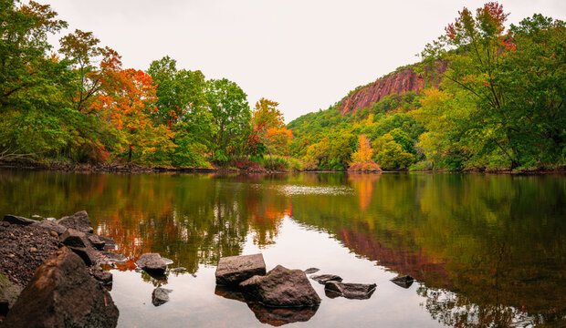 Beautiful fall woodland with rocks and reflections in the river water. Tranquil autumn forest image with space for texts and design. Mill River landscape at East Rock Park in New Haven, Connecticut.