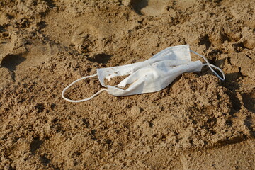 Old anti virus mask thrown on the beach sand. A blue disposable face mask found on the beach during COVID-19 pandemic.