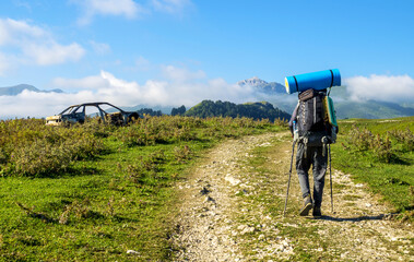 a tramp with a backpack walks along the road past an old car