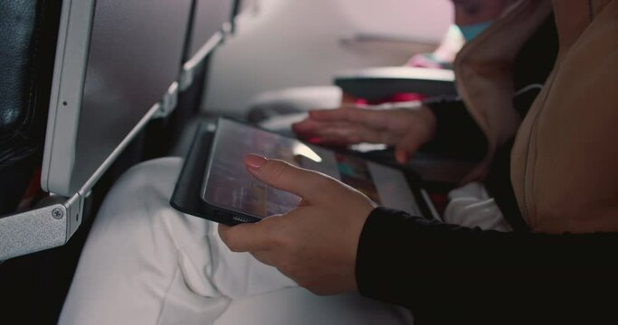 A young woman of caucasian appearance makes a flight on an airplane, a teenager uses a phone on an airplane, scrolls through pictures, messages, opens an application.