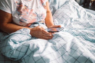Woman hand using mobile phone checking social media network feed or message chat sitting in bed at home.