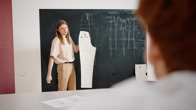 Fashion industry education. Young professor explaining clothes making process to students, talking with pants pattern