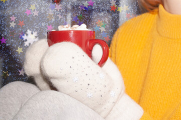 A Christmas red mug in the background with mittens and candles.