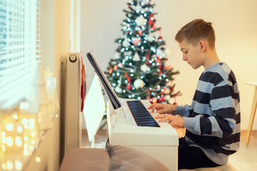 Tennage boy practise plaing piano with new years tree on background