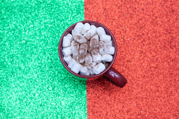 Christmas cup with marshmallow on red and green backgrounds.