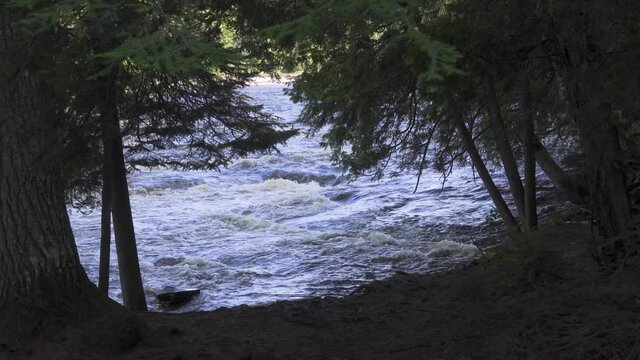 River flowing between banks of trees in northern Michigan in late summer--view of the river through a clearing between trees; blue water, green trees. 275
