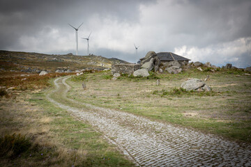 a cobbled road and a windfarm on a mountain landscape near Sao Pedro do Campo Chapel, Casais (Tendais), Cinfaes municipality, Viseu, Portugal - obrazy, fototapety, plakaty