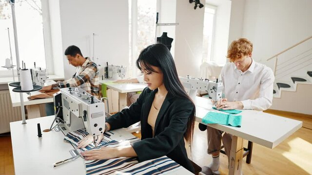 Tailor atelier. Group of young multiethnic fashion designers making new clothes , sewing on sewing machines at workshop