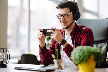 Creative man looking at screen typing message with smartphone. Young man relaxing using laptop computer working and video conference meeting. Business concept.
