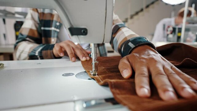 Dressmaking process. Close up shot of unrecognizable man tailor sewing brown velveteen fabric on sewing machine