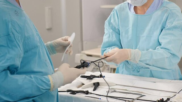 Part of surgical laparoscopic surgery in clinic. Nurse in operating room passing sterile laparoscopic instrument from hand to hand. health and medicine. Hands of surgical nurse picking up instrument