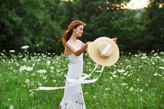 Woman in white dress hat holding flowers nature walk