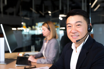 Close-up photo, portrait of Asian male employee contact center, round-the-clock online customer support, employee looks at camera and smiles