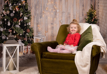 kleines Mädchen mit blonden Locken auf grünem Sofa sitzend vor Christbaum
