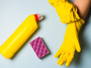 housewife putting on yellow latex cleaning gloves on blue background with copy space