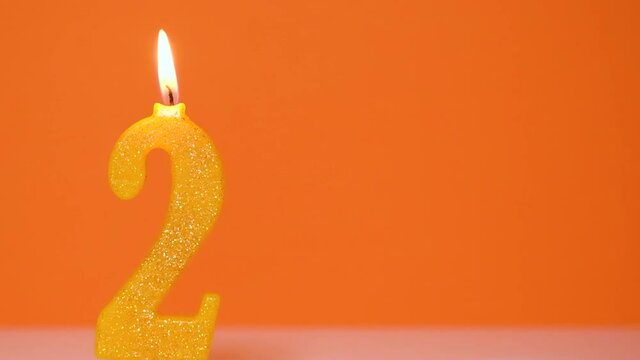 Anniversary video banner with Burning golden number two candle on orange Background. Full HD resolution anniversary banner with copy space.