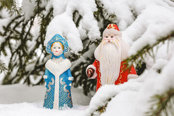 Christmas decorations (Russian Santa Claus and Snow Maiden) standing under the snowy Christmas tree. New Year, holiday background.