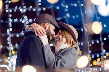 Christmas couple hugging on the street surrounded by lights on Christmas eve. Happy, romantic lovers hugging on the street surrounded by Christmas lights on New Year's eve.