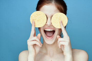 woman with sponges in hands bare shoulders clear skin blue background