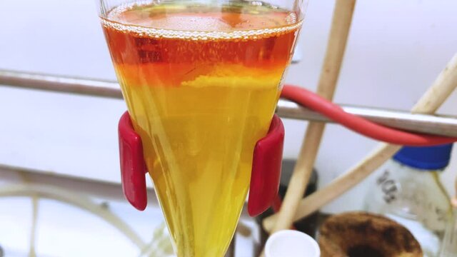 Separation of organic layer and water layer in separating funnel in a chemistry lab for education purpose. Effervescent of carbon dioxide bubble in organic layer. 4K scientific background concept.
