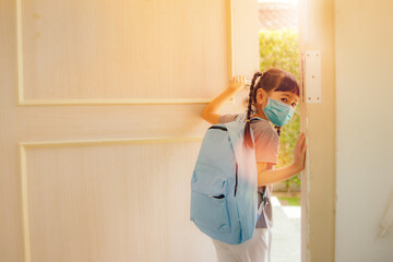 Asian school girls wear masks to protect against COVID-19 and carry a backpack to open the doors of...