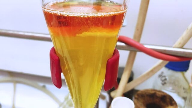 Separation of organic layer and water layer in separating funnel in a chemistry lab for education purpose. Effervescent of carbon dioxide bubble in organic layer. 4K scientific background concept.